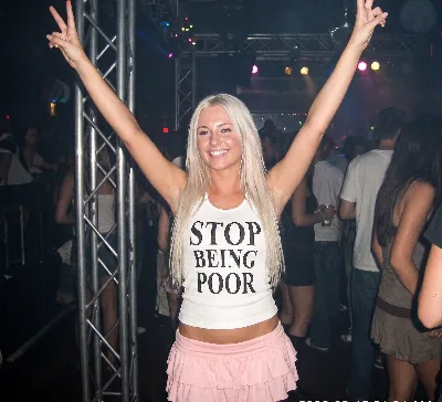 Blonde party guest in a shirt that reads Stop Being Poor